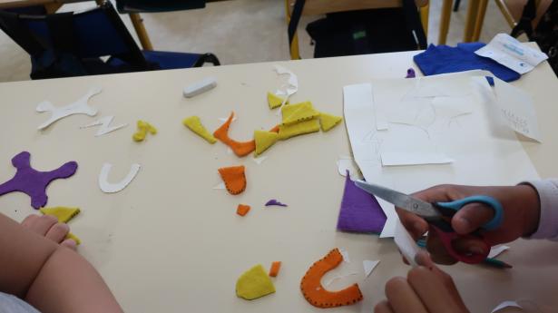 les enfants découpent les formes colorées qui composeront leur personnage, dans de la laine préfeutrée par Clotilde
