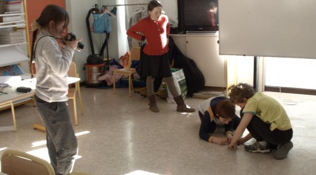 Lorelei reprend son image en photo en la mettant en scène à l'aide de ses camarades. L'image qu'elle est en train de prendre illustre une histoire écrite par Estéfan, présent dans la photographie.